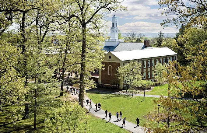Drew University campus with students walking on a path, surrounded by trees and a building.